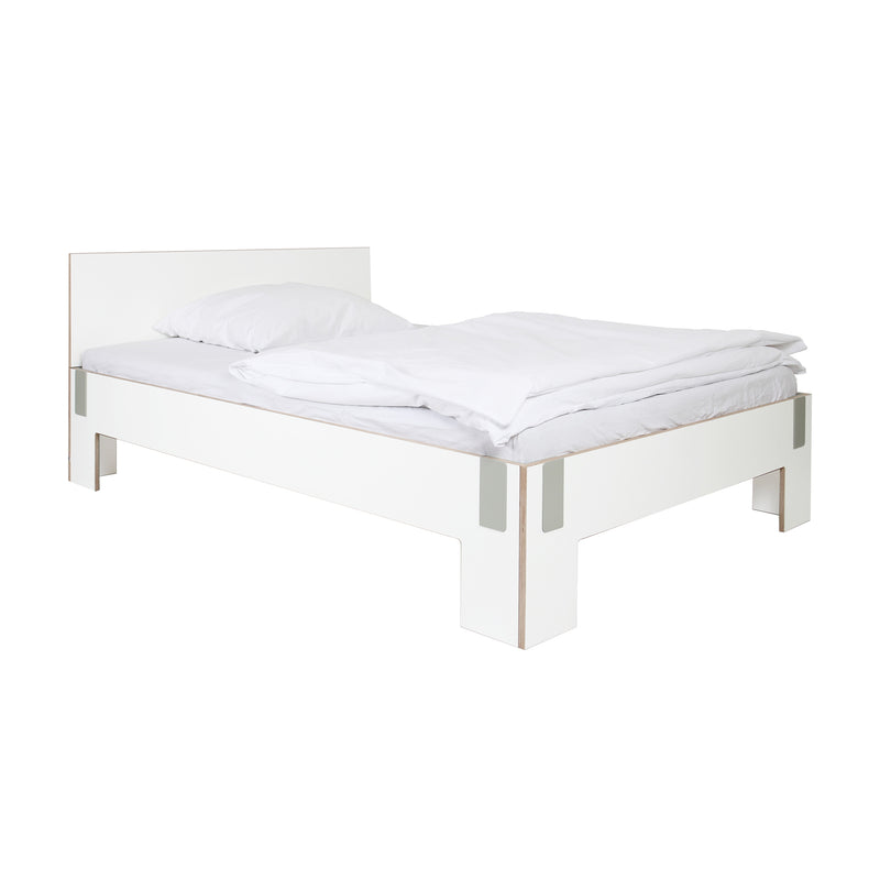 The Moormann Tagedieb bed, set against a white backdrop, showcases a minimalist design with a simple headboard and elegant white bedding. It offers adjustable mattress support for personalized comfort.
