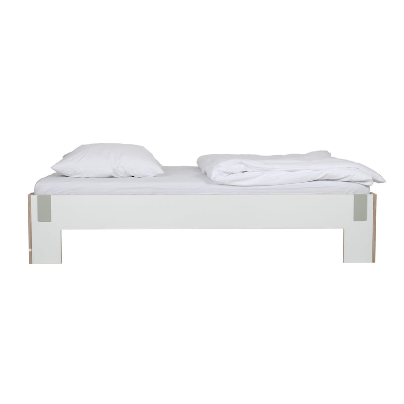 The Tagedieb bed by Moormann offers a minimalist white platform design, complemented by two pristine pillows and an elegantly draped duvet. Set on a simple white backdrop, it features an adjustable mattress support for enhanced comfort.