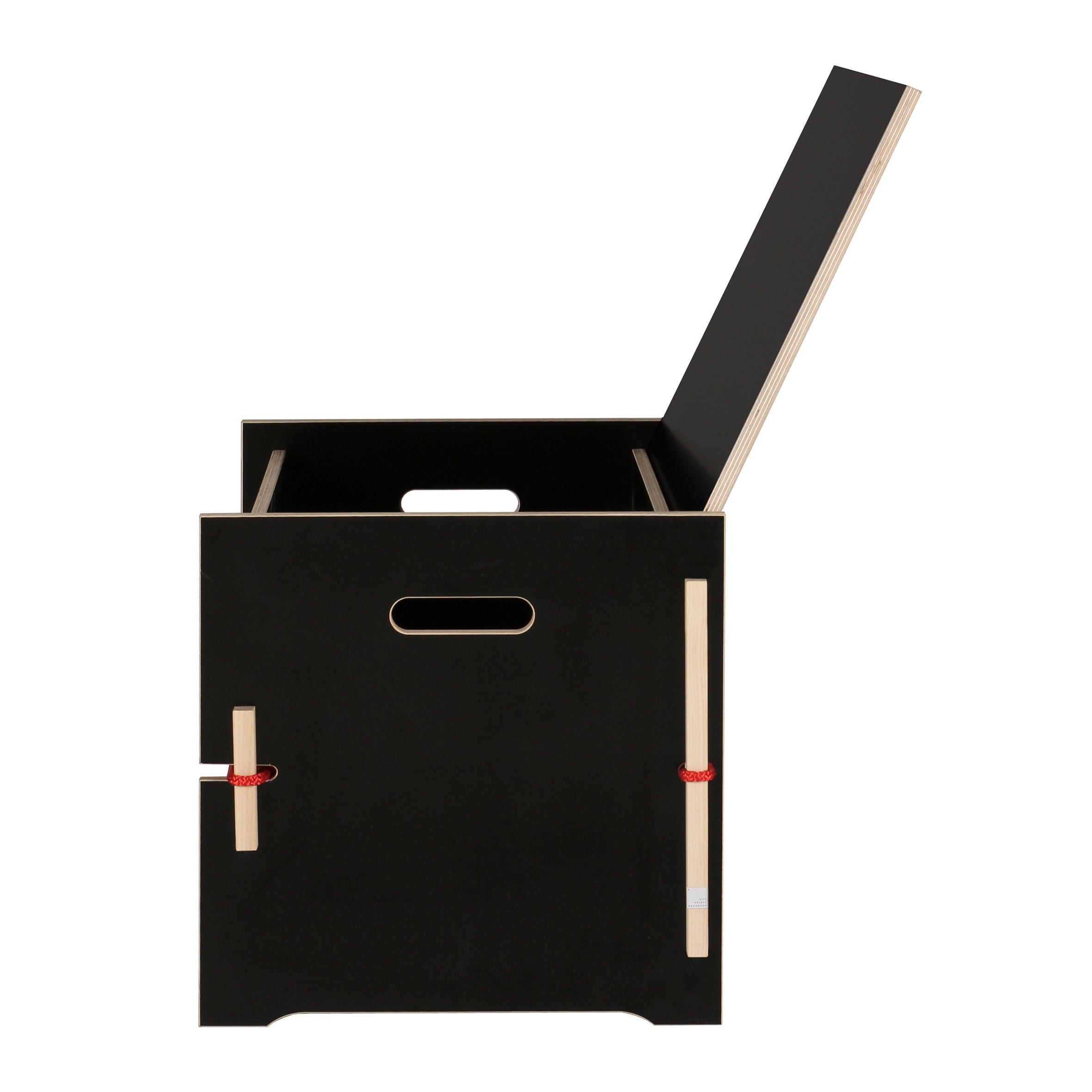 The Trude by Moormann is a black wooden storage box with a hinged lid, cutout handles, and a red strap securing the front panel. Its small legs elevate it for an elegant storage solution, perfect for bed linen.