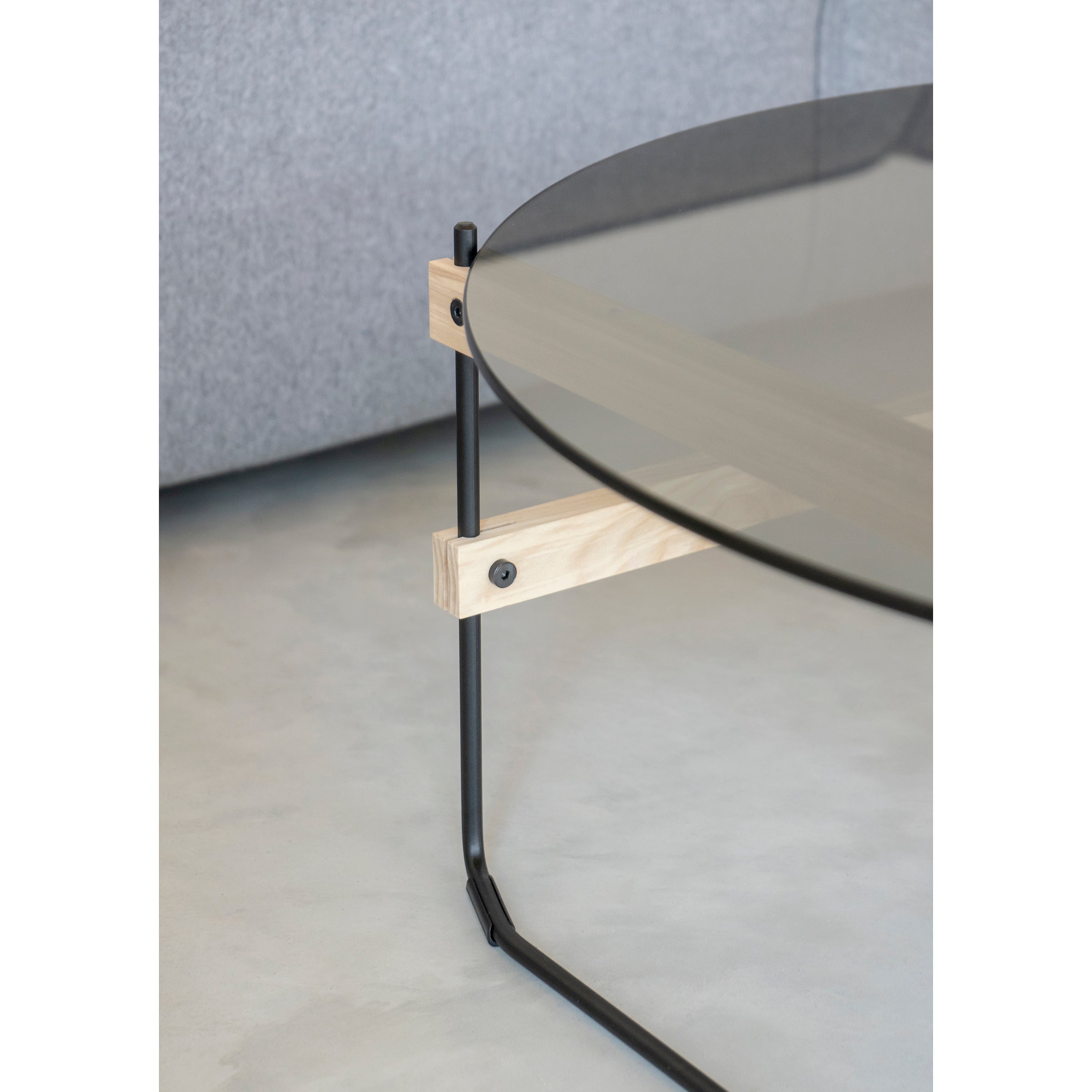 The Netto Coffee Table by Moormann features a grey tinted ESG glass top with a metal and light wood frame. Its minimalist design pairs beautifully with a gray fabric sofa and Lounge Chair Brutissimo on the light gray concrete floor.