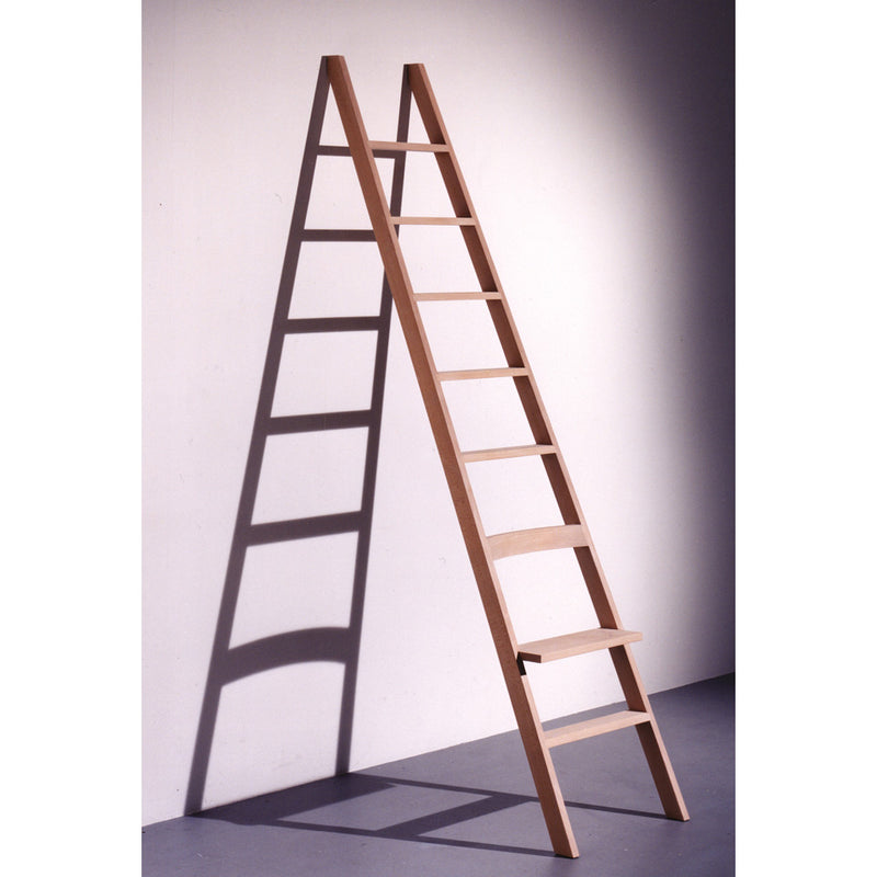 A Hochacht A-frame ladder by Moormann, made from untreated beech, leans against a white wall. With evenly spaced rungs, it casts a shadow on the smooth gray floor.