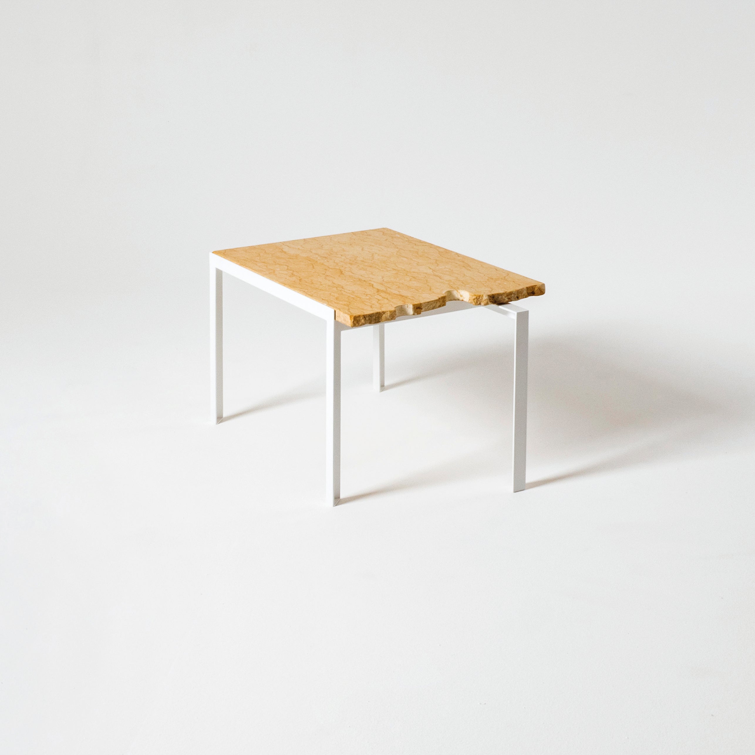 The Petite Table DAngle by Atelier Haussmann features a wooden top with a natural finish and slightly irregular edge, complemented by sleek white metal legs, all set against a plain white background.