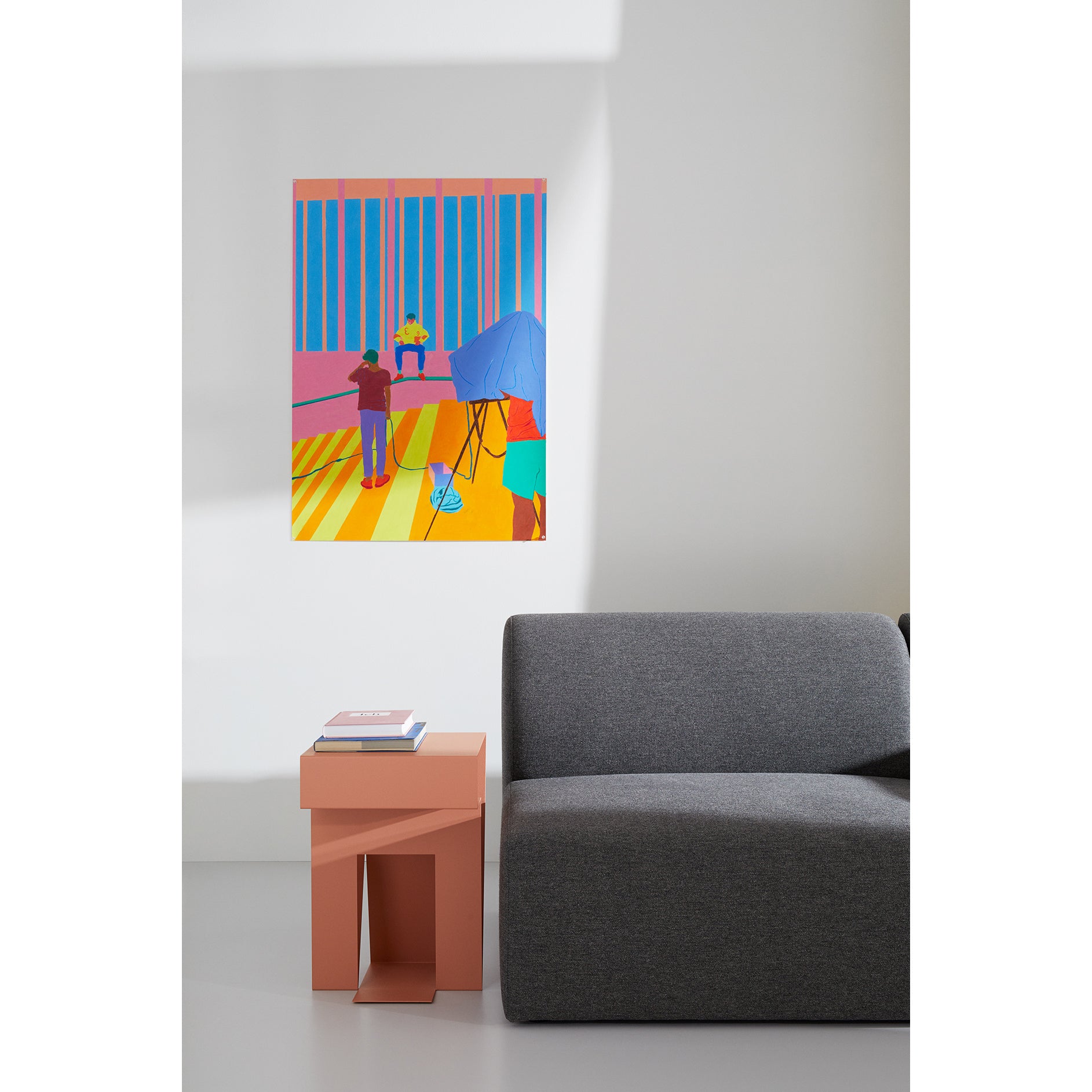 A modern living room features a gray sofa and a pink Neumann Sidetable by Objekte unserer Tage. A vibrant abstract painting with vertical stripes and figures adorns the wall above, casting a diagonal shadow on the white wall, highlighting the meticulous design process of this artful space.