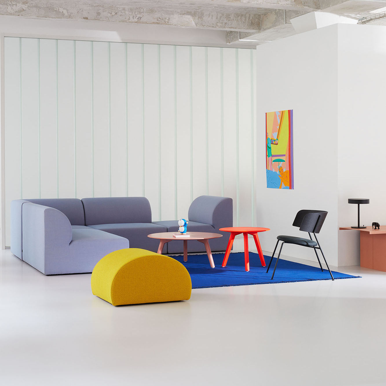 The modern living room showcases an Objekte unserer Tage Weber Modular Sofa in gray, paired with a yellow ottoman and red side table. A black chair sits on a blue rug by a small coffee table with decor. A colorful abstract painting adds flair to the white wall, embodying sustainability and minimalist design.