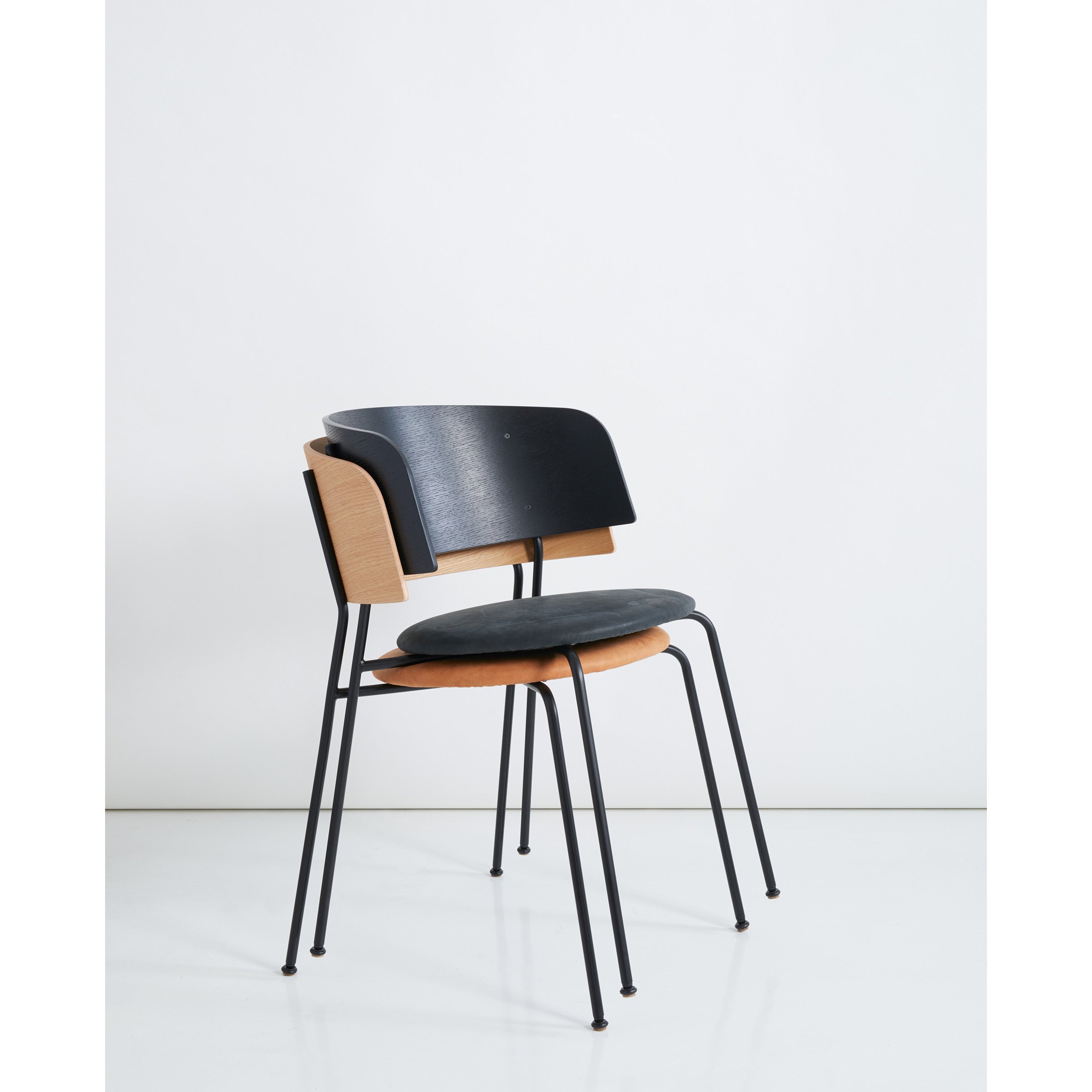 The Objekte unserer Tages Wagner Armchair blends modern design with a sleek black powder-coated steel frame, wooden backrest, and seat with black cushions. Its minimalistic wood-metal fusion is elegantly set against a plain white backdrop.