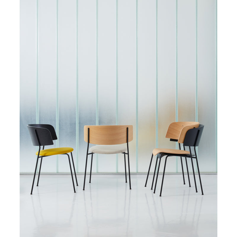 Three modern chairs with black metal legs are set in a minimalist space. Two have wooden backs; one has a black backrest. The seats are black, cream, and yellow. Included is the Wagner Armchair by Objekte unserer Tage. A frosted glass wall serves as the chic backdrop to this display.