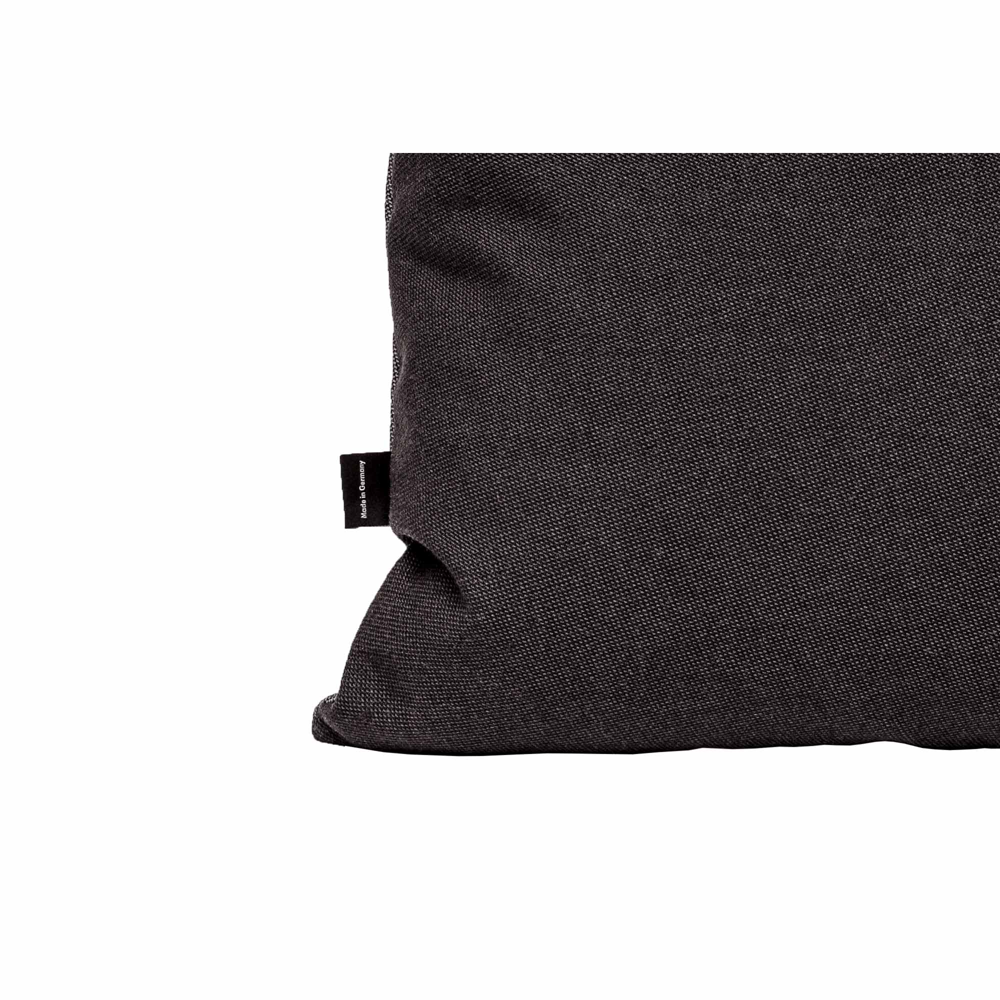 A Weber Cushion by Objekte unserer Tage, detailed with exquisite textures from premium fabrics and leathers, features a small black tag on its left side. Its set against a plain white background occupying the right half of the image.