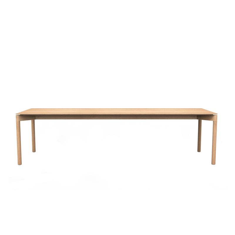 The Wedekind Table by Objekte unserer Tage is a long, rectangular wooden table with a minimalist design, crafted from sustainable oak wood. It features straight legs and a smooth surface, with its light tone elegantly standing out against a plain, dark backdrop.