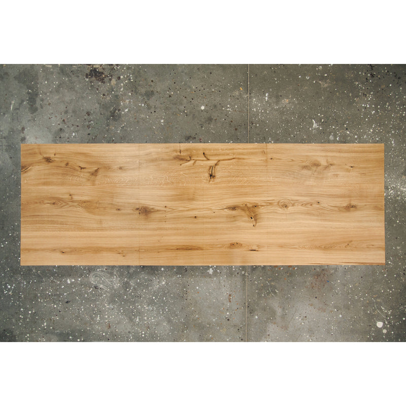 The Join Extendable Table by One For Hundred, crafted from solid wood with a light natural finish and visible grain patterns, rests on a speckled gray concrete floor. Its clever synchronous extension mechanism ensures easy adaptability for any occasion.