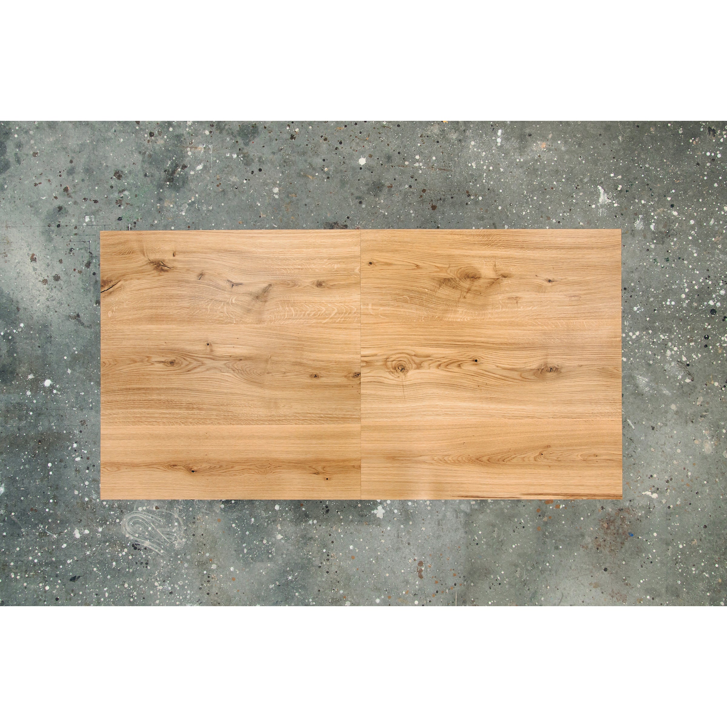 The Join Extendable Table by One For Hundred is an elegant rectangular piece with a light brown finish that highlights natural grain patterns and distinct knots. Its solid wood construction and extendable design sit gracefully on a speckled concrete floor, adding sophistication to any space.