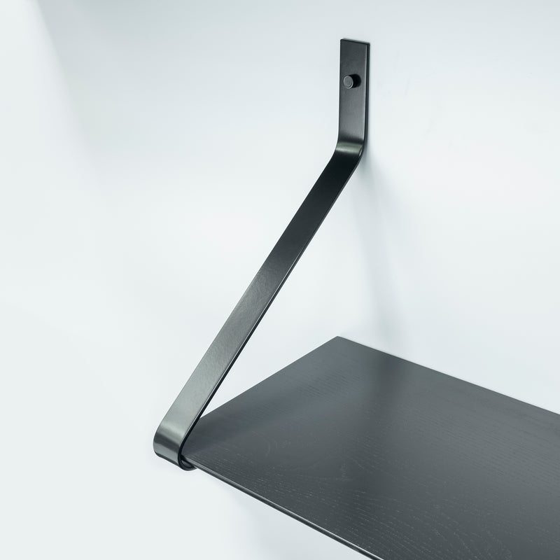 The Ribbon Shelf by One For Hundred showcases a minimalist design with powder-coated steel brackets holding a dark wooden plank against a plain white background.