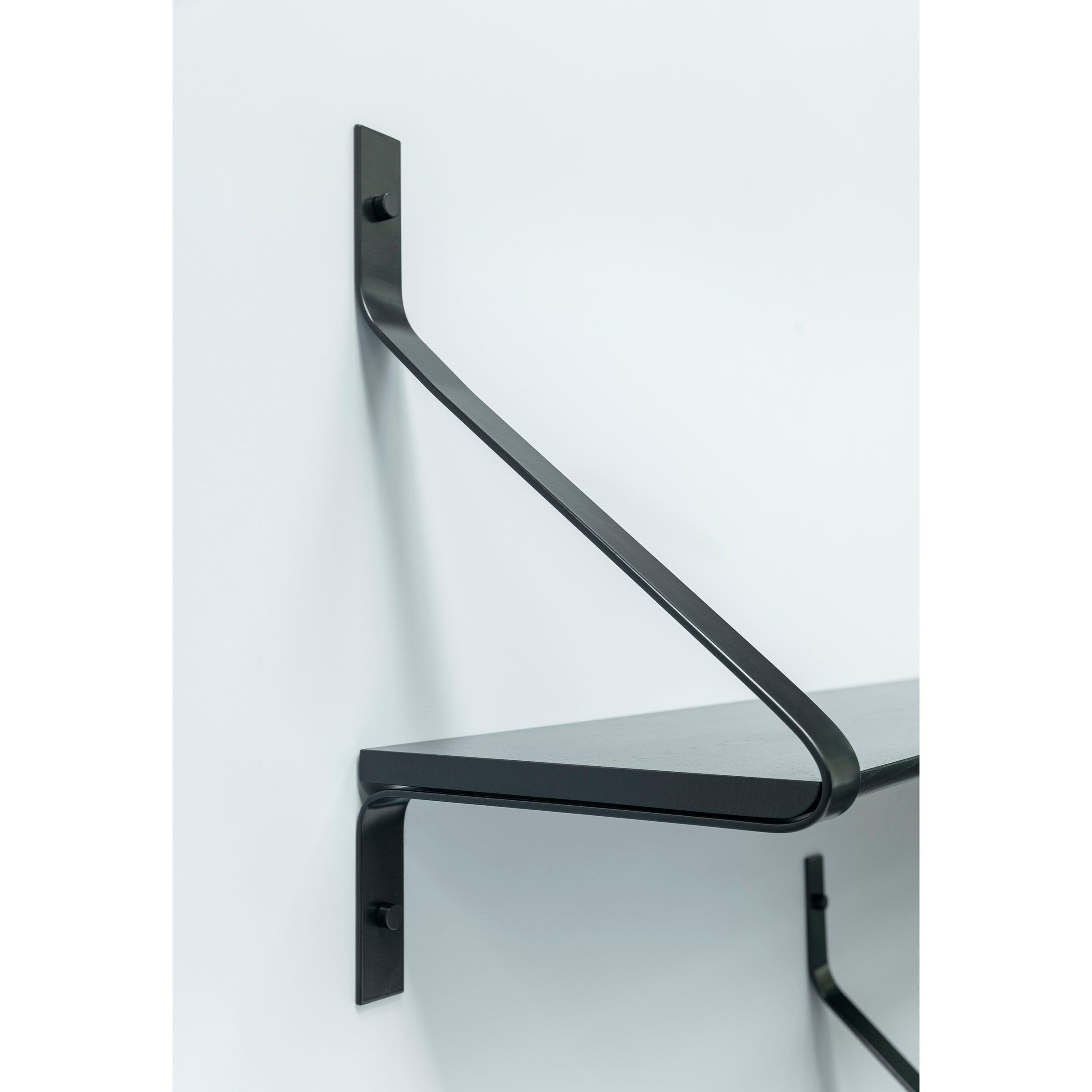 The Ribbon Shelf by One For Hundred, features a minimalist design with a black metal diagonal support bracket, mounted on a white wall. Its sleek and modern look complements contemporary spaces beautifully.