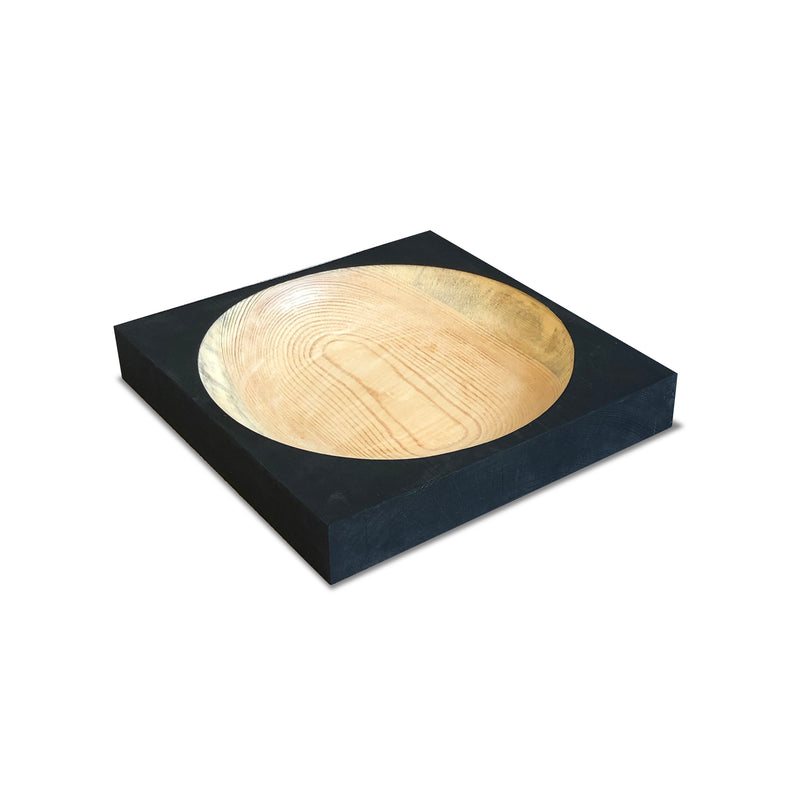 The Cavetto by One For Hundred is a modern pinewood dish with a light grain in a matte black square block. Its smooth, rounded interior contrasts the blocks edges, creating a minimalist table accessory.