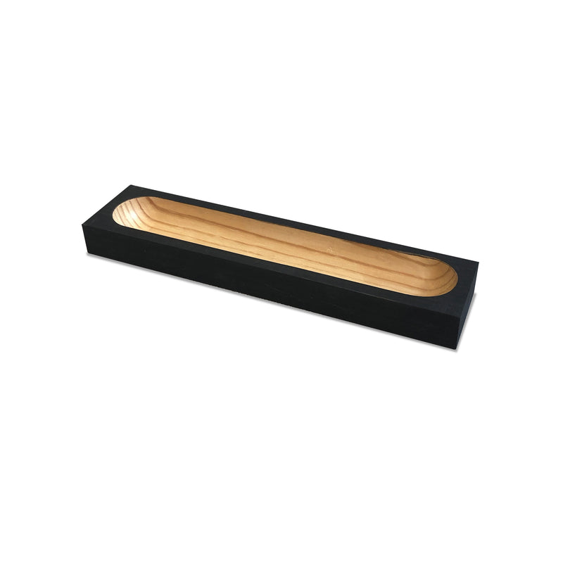 The Cavetto by One For Hundred is a rectangular pinewood display tray with a black exterior and natural wood interior, featuring a central long oval indentation. Its an elegant accessory ideal for holding or organizing items.