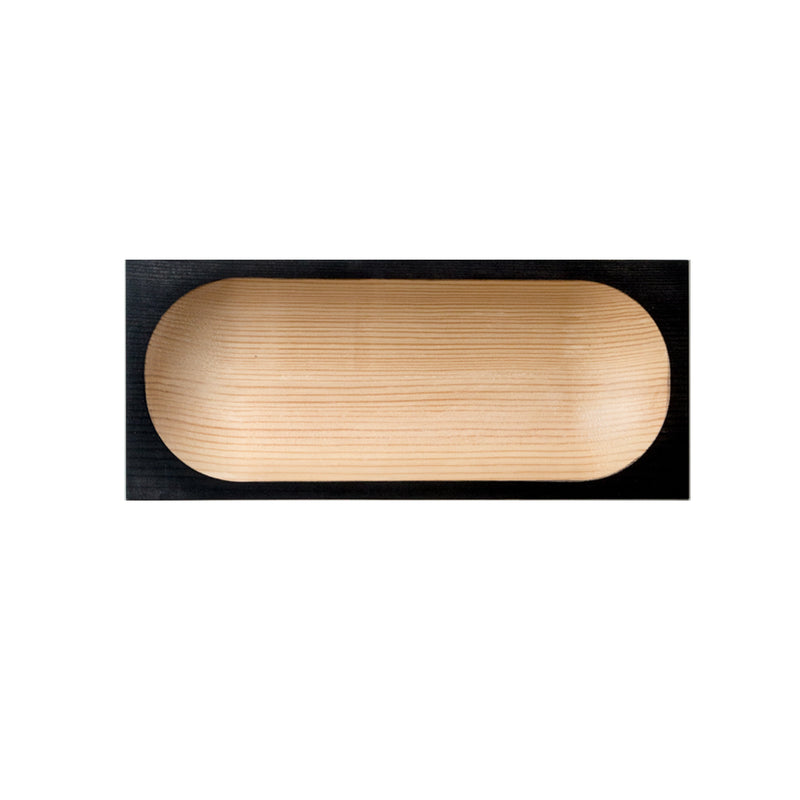 The Cavetto tray by One For Hundred is a rectangular pinewood table accessory with a dark-stained border resembling cavetto molding. It features an elongated oval indentation highlighting the natural wood grain, set against a plain white background.