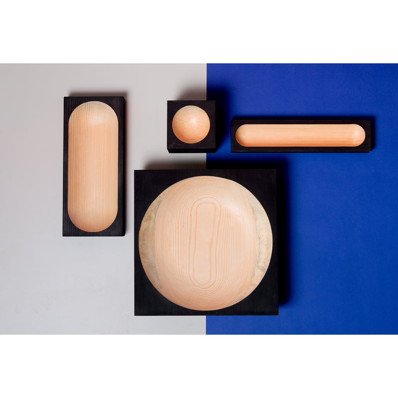 A collection of light pinewood bowls by One For Hundred, featuring Cavettos detailed square black frames, rests elegantly on a surface split into gray and blue sections, enhancing the scene with natural elegance.