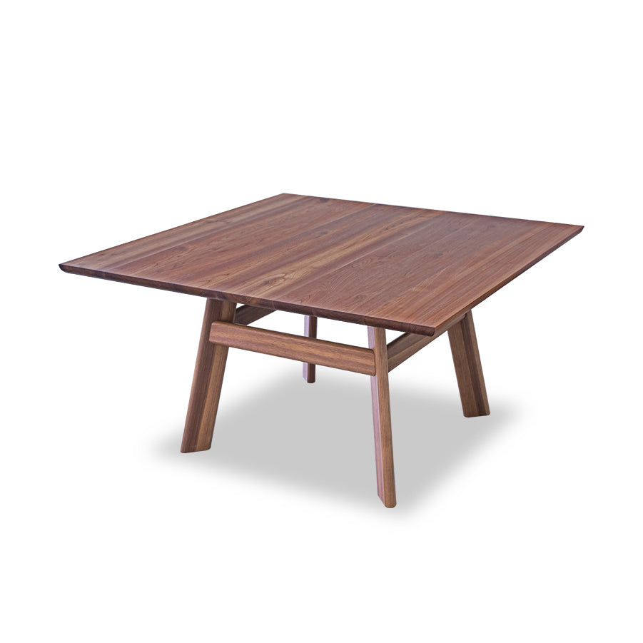 Meet the YOGI Table by One For Hundred: A square, minimalist design featuring four angled legs. Made from solid wood, it boasts a smooth, polished surface that highlights its natural beauty.