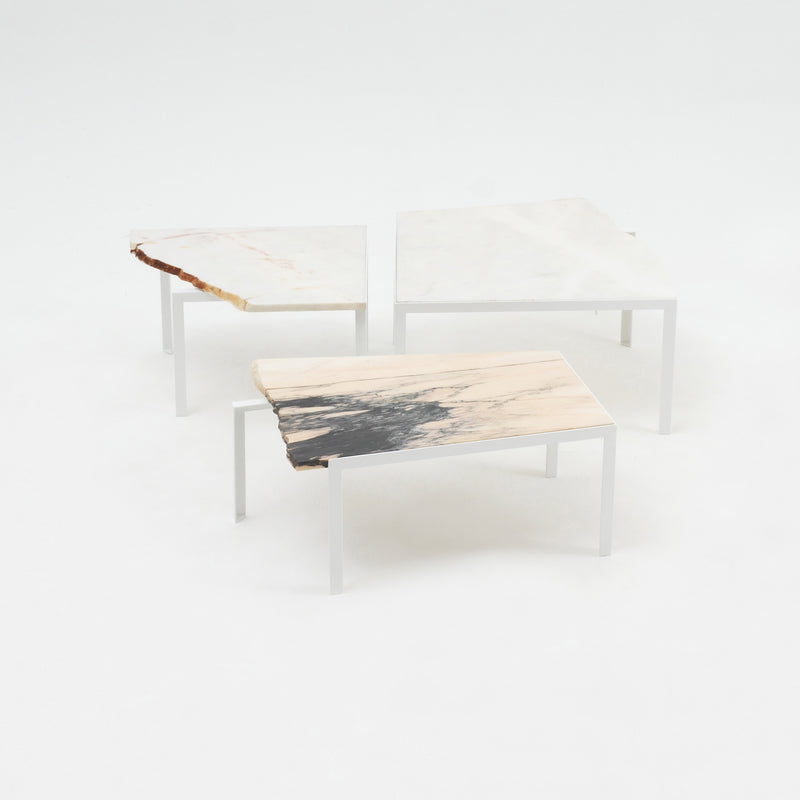 Three Petite Table DAngle tables by Atelier Haussmann feature irregular marble tops in white, beige, and gray hues. Each has a minimalistic steel angle frame with legs, highlighting abstract patterns on remnant marble slabs, clustered on a plain background.