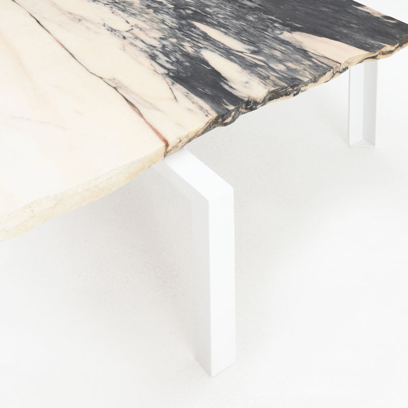 The Petite Table DAngle by Atelier Haussmann features a rectangular remnant marble slab top with black and beige veining, set on clean, white metal legs. It stands on a light-colored floor and highlights a minimalist design.