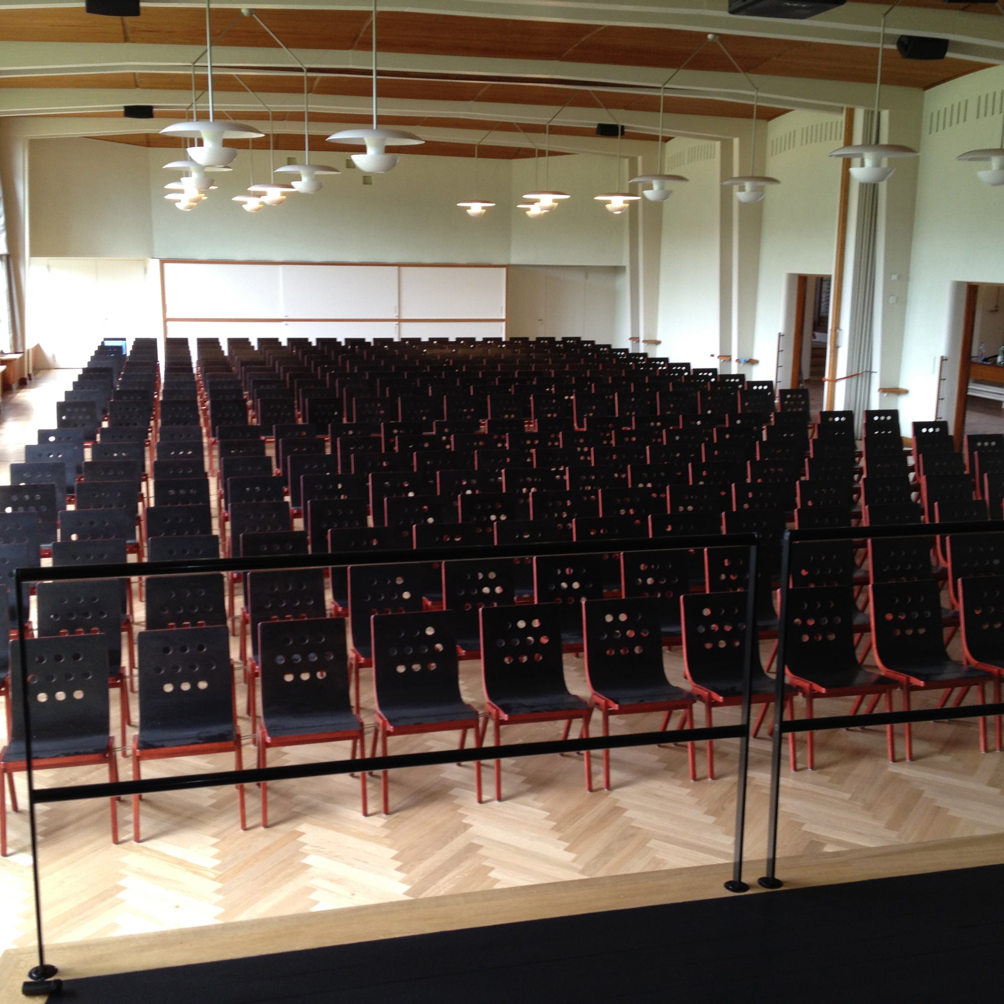 4/5/4 Armchair shown in rows in an auditorium setting, black seats with red frames on herringbone wood flooring