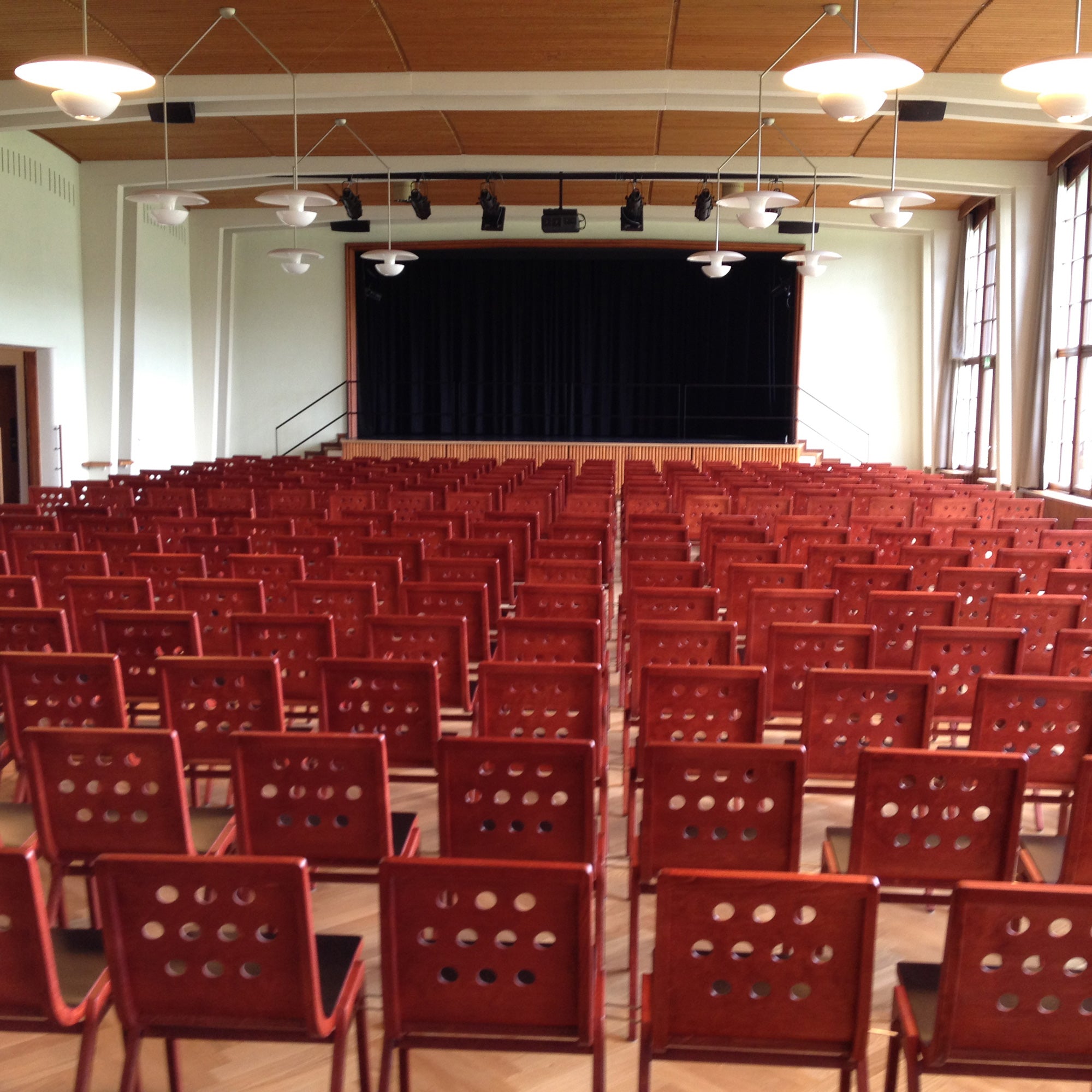 Rows of red 4/5/4 Armchairs by Roland Rainer arranged in an auditorium facing a stage with theater lighting