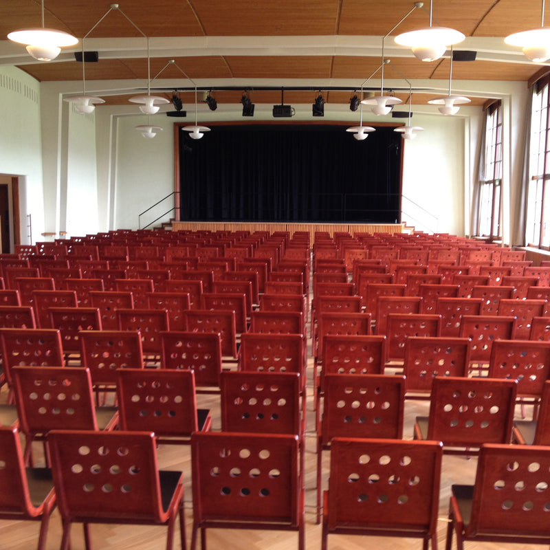 Rows of red 4/5/4 Armchairs by Roland Rainer arranged in an auditorium facing a stage with theater lighting