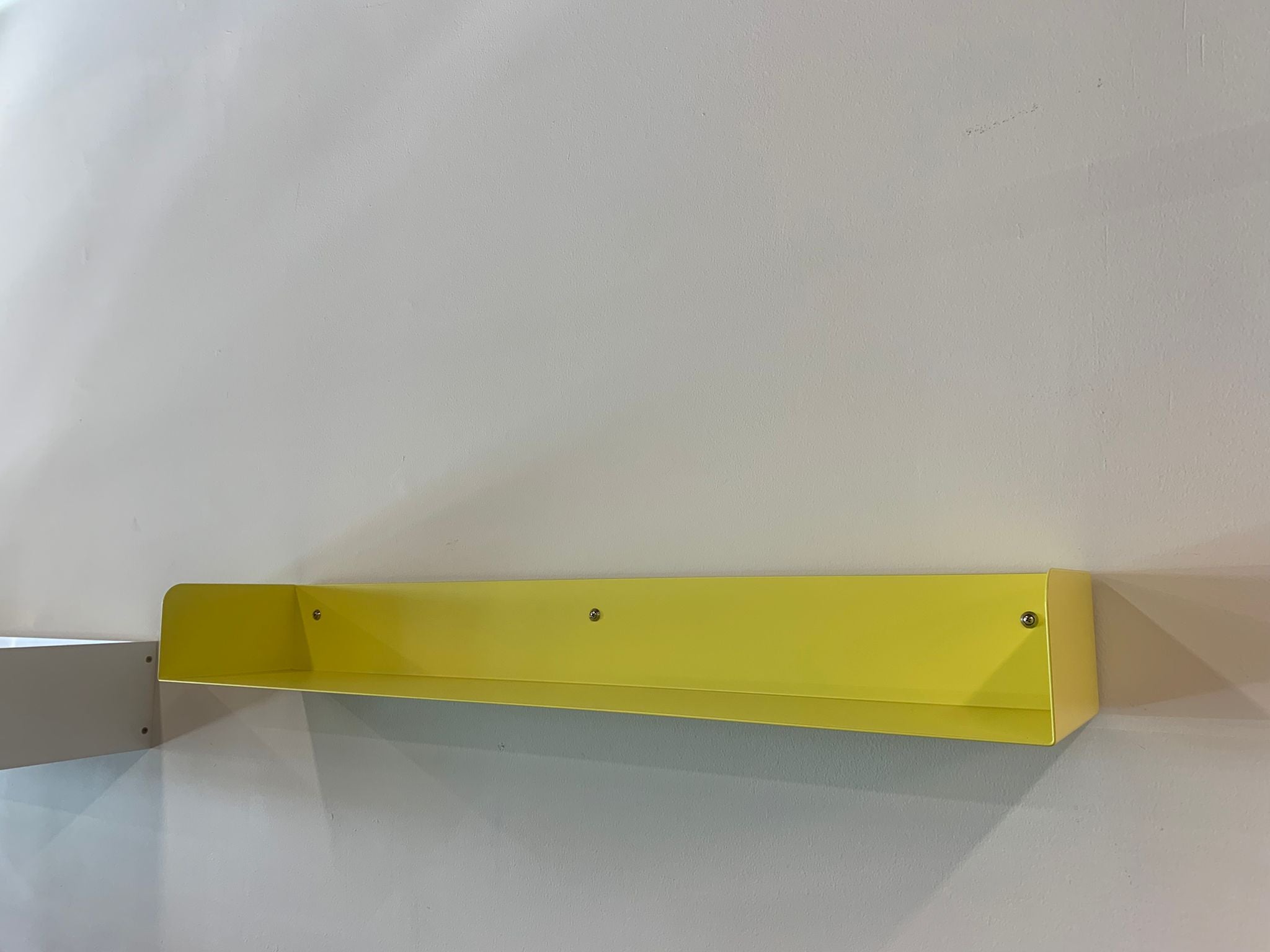 A sulfur yellow Poggibonsi Shelf by Atelier Haussmann is mounted on a white wall, casting a faint shadow to the right. Its minimalist design combines elegance and simplicity.