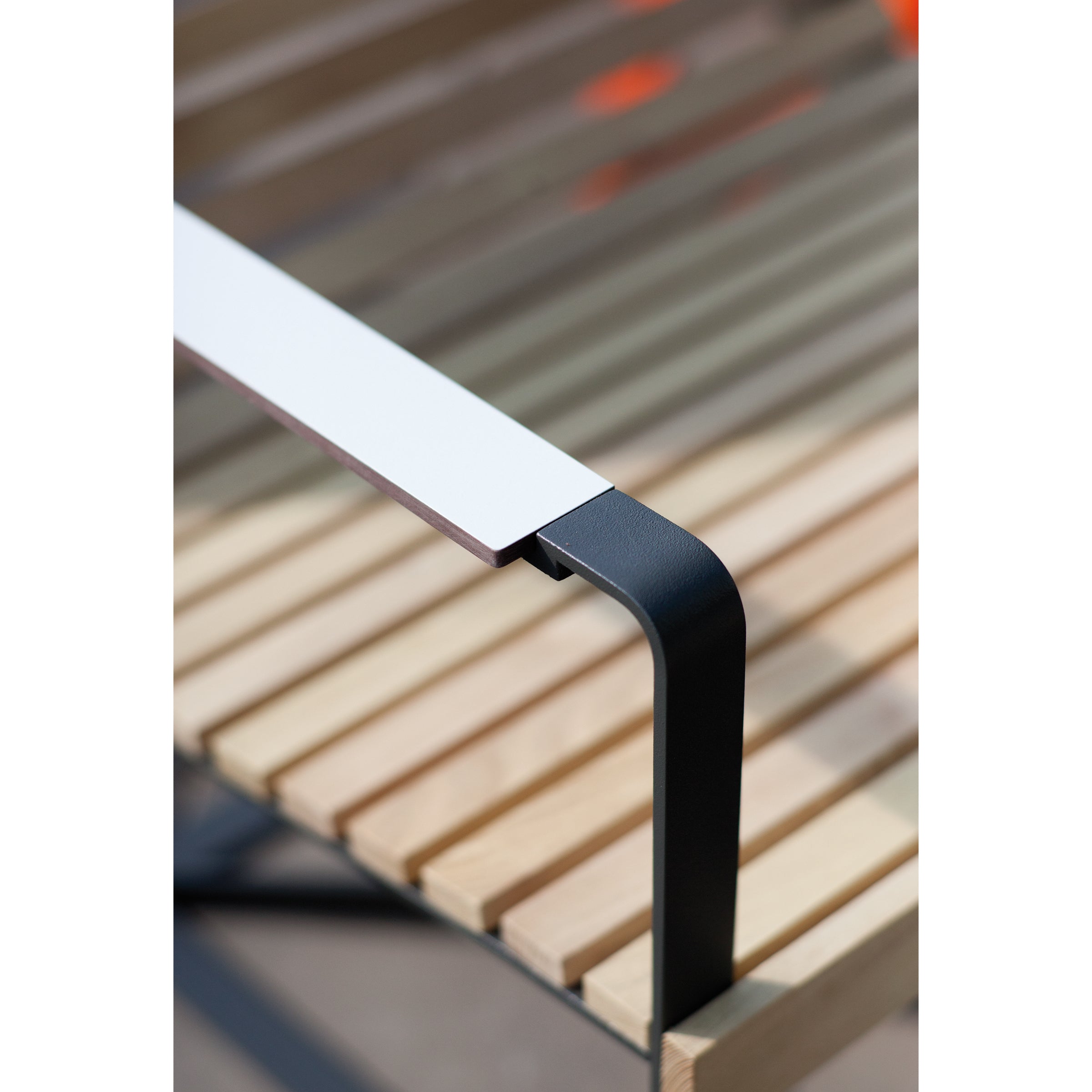 Close-up of the Preva Armchair by Egoe, featuring slatted wooden seating and a sleek metal armrest painted black and white. The elegant curve of the armrest enhances its modern, minimalistic design.