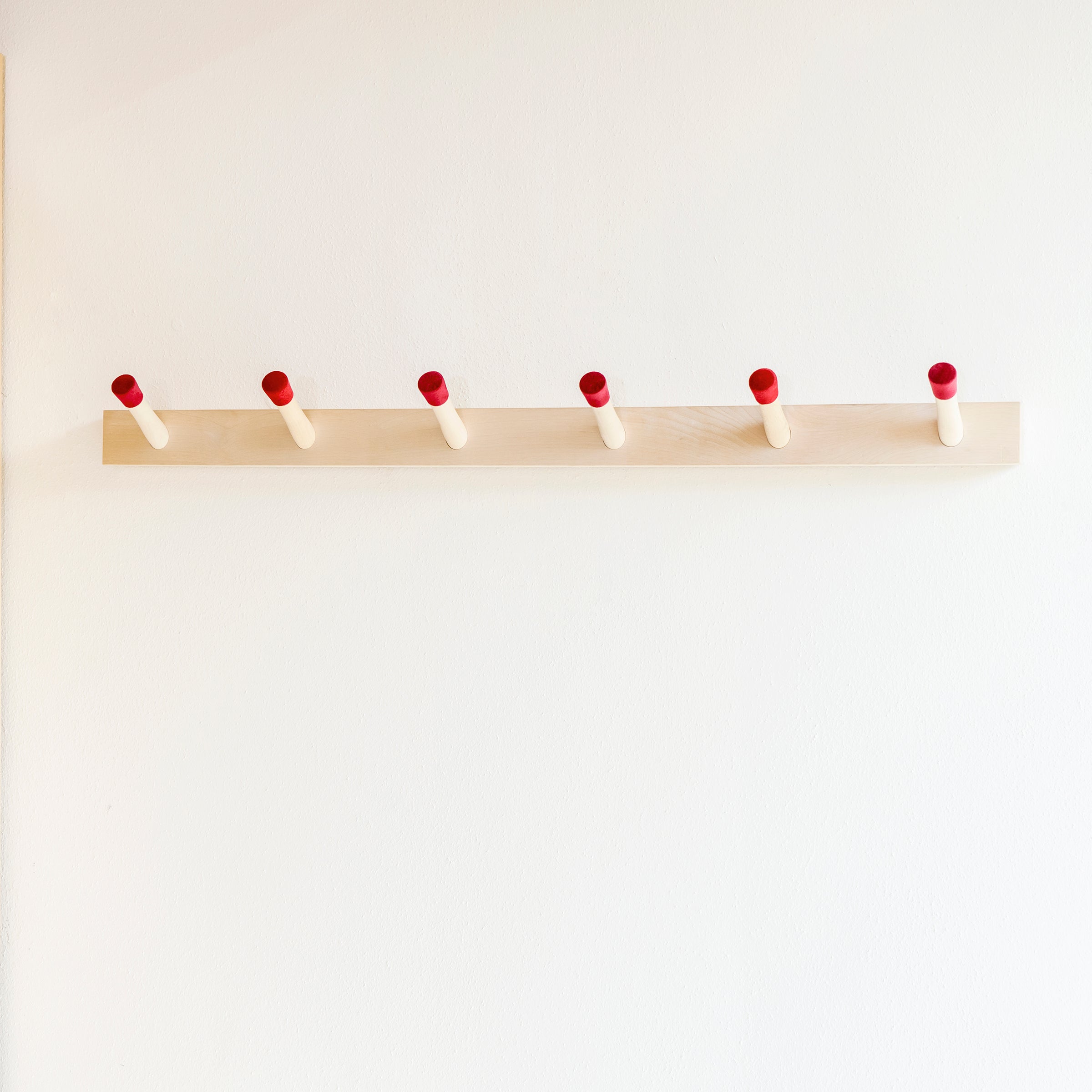 The Rechenbeispiel by Moormann is a sleek birch plywood coat rack featuring six evenly spaced pegs with red tips, mounted on a white wall to add style and functionality.