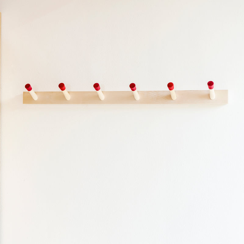 The Rechenbeispiel by Moormann is a sleek birch plywood coat rack featuring six evenly spaced pegs with red tips, mounted on a white wall to add style and functionality.