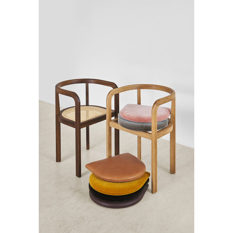 Two RH01 Stuttgart wooden chairs from E15 are showcased. The left chair has a woven seat, and the right features a pink cushion with four colorful teardrop-shaped cushions below. This scene reflects the elegance of Richard Herre design against a plain white wall.