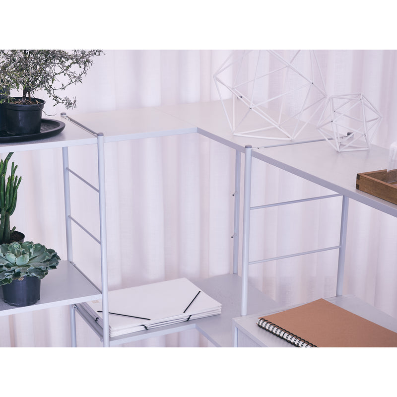 The DHS10 Shelf by Richard Lampert, inspired by Herbert Hirches German industrial design, showcases potted plants, a geometric wire sculpture, folded papers, and a spiral notebook. Light-colored curtains in the background enhance its bright and airy atmosphere.