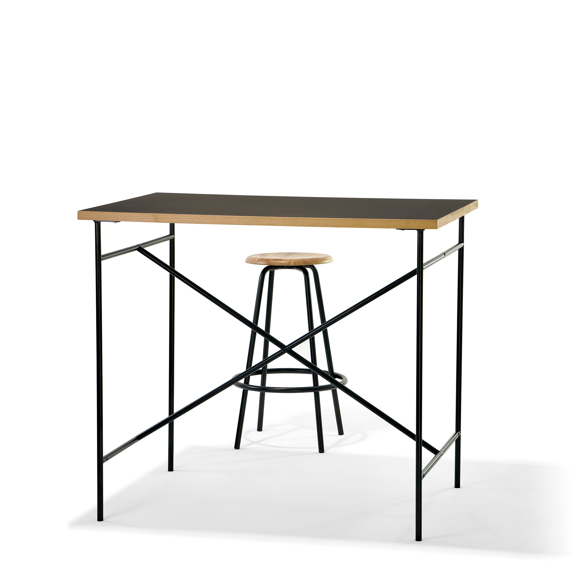 The Richard Lampert Milla High Table 1100 is a minimalist tall desk with a black metal frame and wooden tabletop, accompanied by a stool with a round wooden seat and metal legs, set against a white background.
