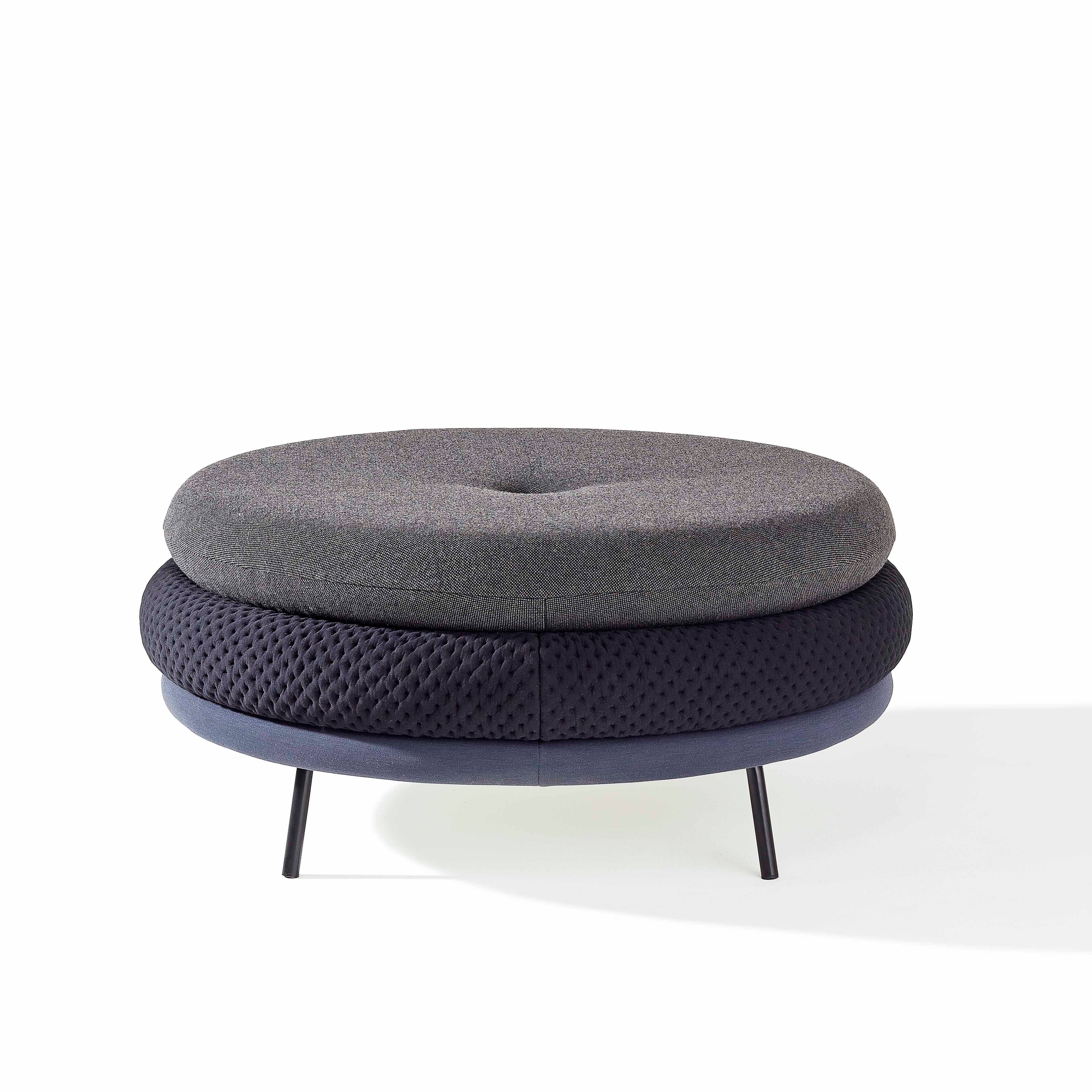 The Fat Tom by Richard Lampert is a modern round ottoman featuring two cushioned layers in gray and black on sleek, thin metal legs. The top is smooth with a textured middle layer, complementing any setting against a plain white backdrop and pairing well with comfortable stools.