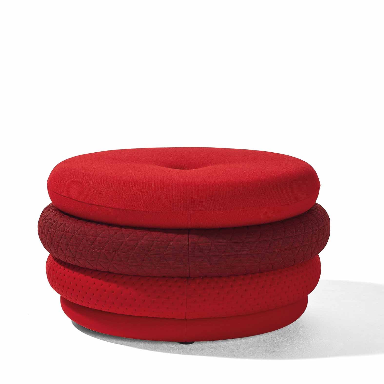 A round, red ottoman called Fat Tom by Richard Lampert sits against a white background. Combinable covers in varying red shades and textures create a stacked look, highlighting the brands talent for crafting comfortable stools with unique flair.