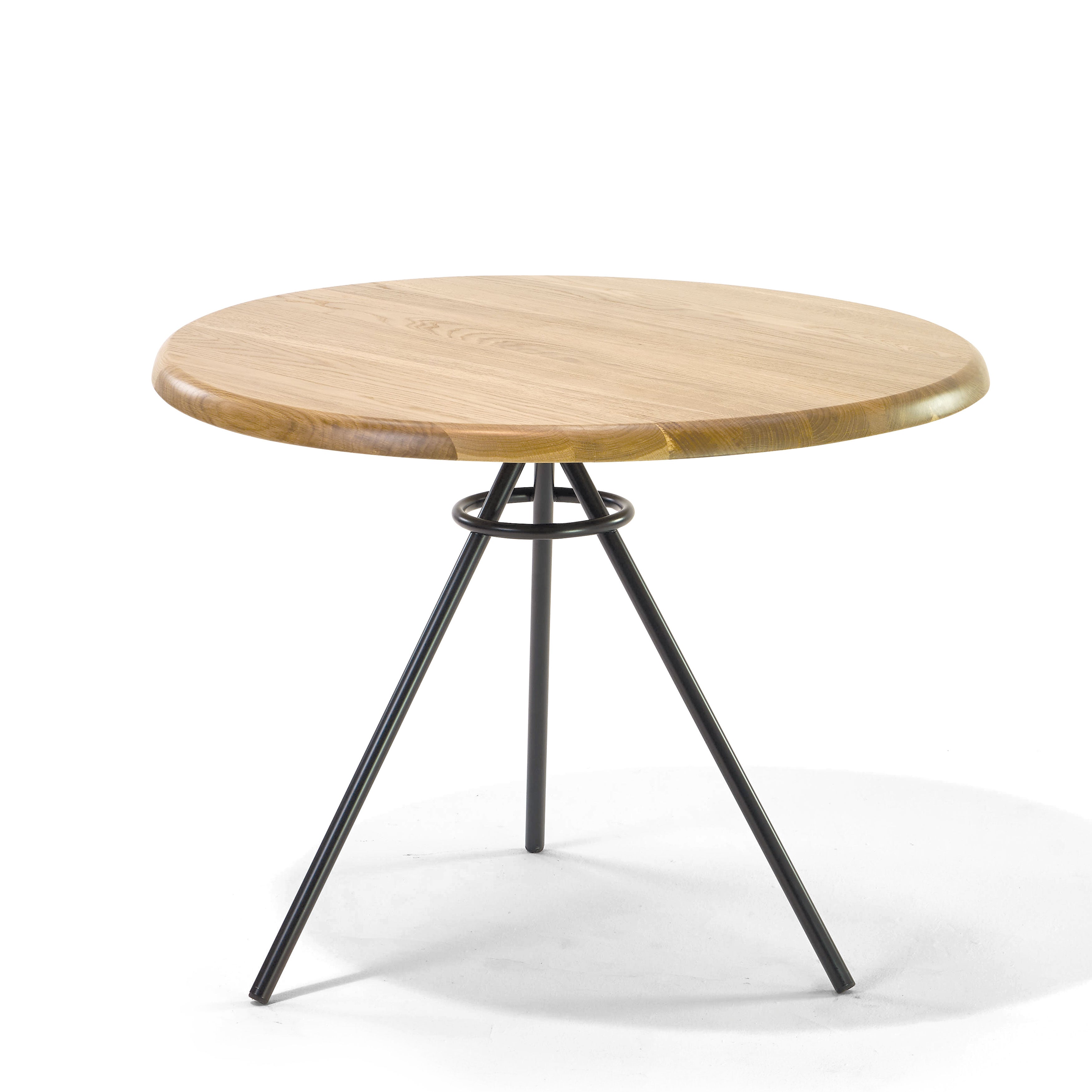 The Tom Bistro Table by Richard Lampert features a round wooden top with a smooth surface, supported by three tubular steel legs that converge at the center to form a stable tripod base, ideal for a dining corner and casting a slight shadow on the white surface below.