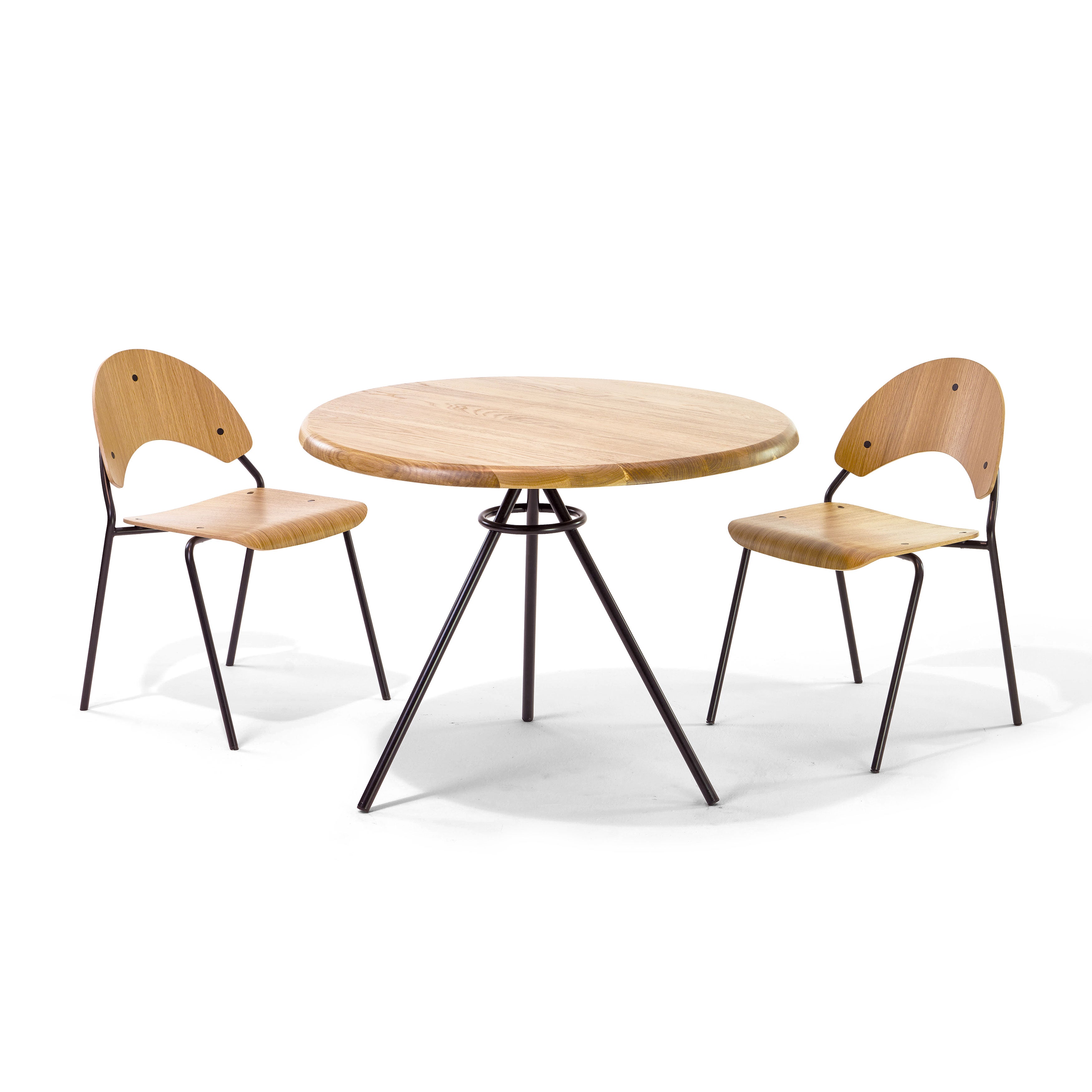 The Tom Bistro Table by Richard Lampert, a round wooden table with a sleek tubular steel tripod base, is complemented by two matching wooden chairs with black metal legs. The chairs have curved backs and two circular cutouts for a modern, minimalist dining corner.