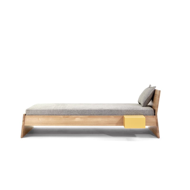 The Stockholm Bed by Richard Lampert is a minimalist birch plywood daybed with a light grey cushion and pillow, designed by Alexander Seifried. It features an attached yellow storage compartment and its sleek design suits contemporary spaces, enhanced by a plain white background.