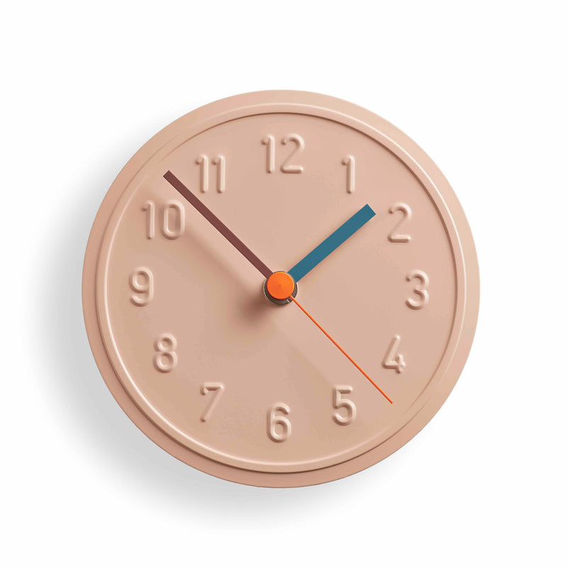 The Alu Alu Wallclock by Richard Lampert, designed by Jochen Gros, is a beige quartz clock with embossed numbers. It features a blue hour hand, brown minute hand, and red second hand on a white background that enhances its shadow effect.