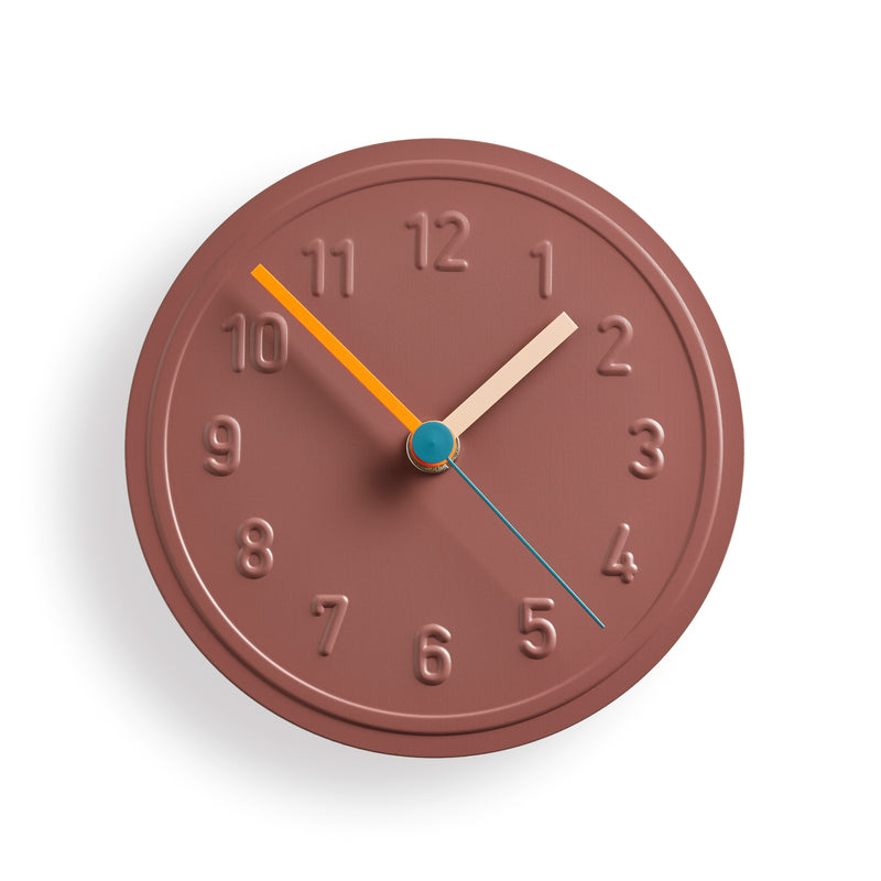 The Alu Alu Wallclock by Richard Lampert, designed by Jochen Gros, is a round, brown quartz clock featuring evenly spaced embossed aluminum numbers and colorful hands: an orange hour hand, a cream minute hand, and a blue second hand.