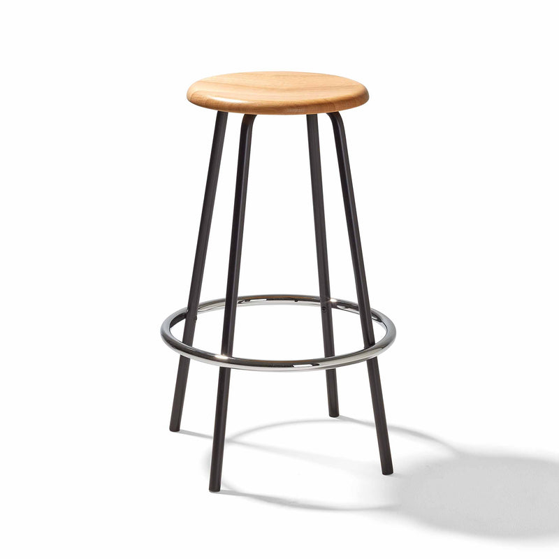 The Richard Lampert Big Tom Barstool has a round wooden seat and black tubular steel legs, with a sleek circular support ring for stability.