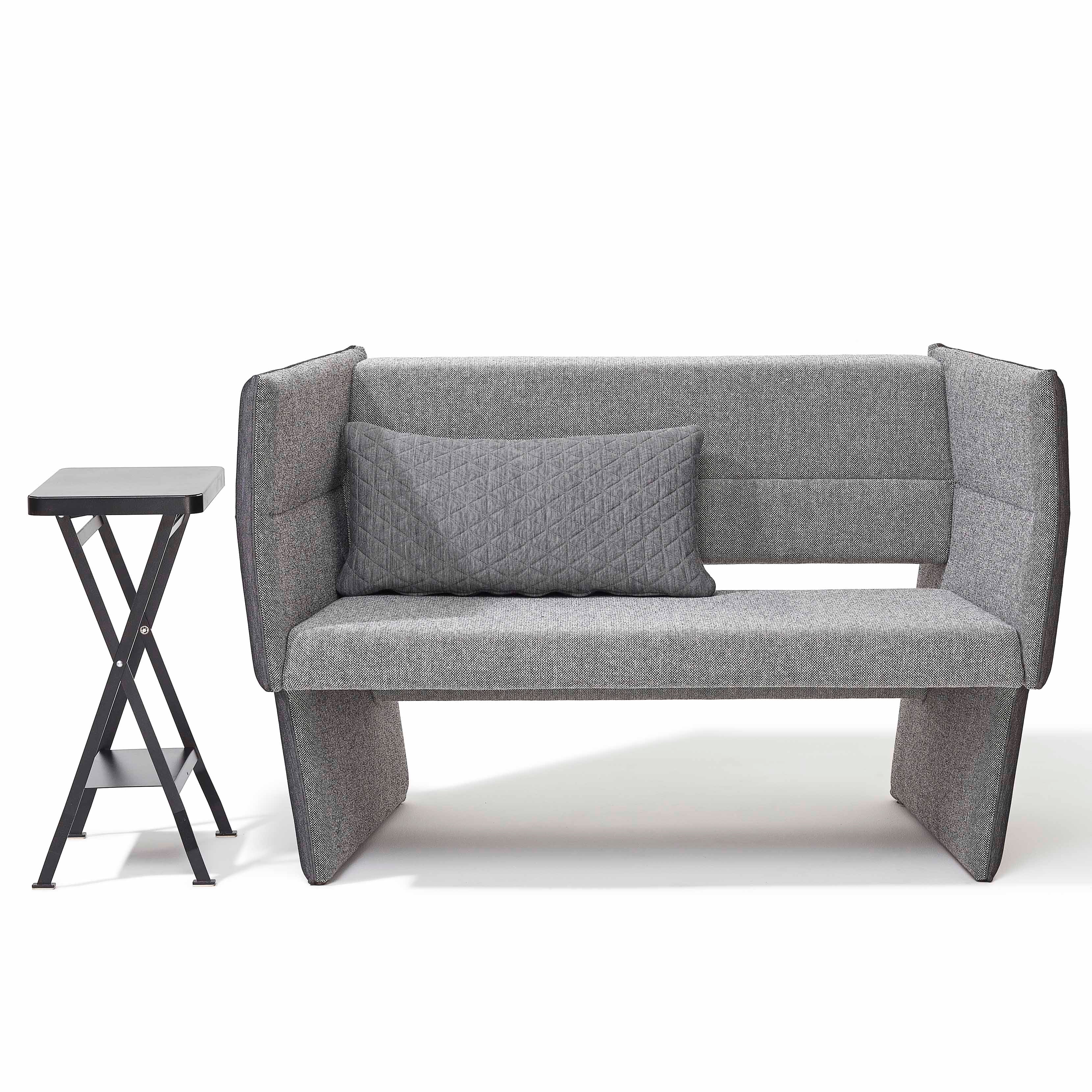 The Cup Sofa by Richard Lampert, a modern gray loveseat with high sides, pairs seamlessly with a small foldable black side table. A textured gray pillow complements the sofa against a plain white background, exuding minimalistic elegance.