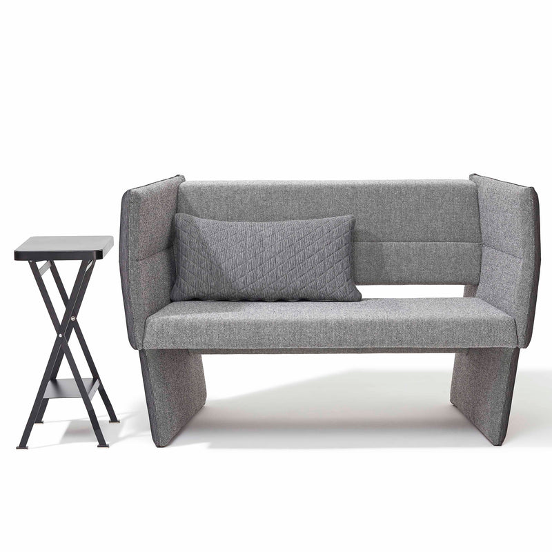 The Cup Sofa by Richard Lampert, a modern gray loveseat with high sides, pairs seamlessly with a small foldable black side table. A textured gray pillow complements the sofa against a plain white background, exuding minimalistic elegance.