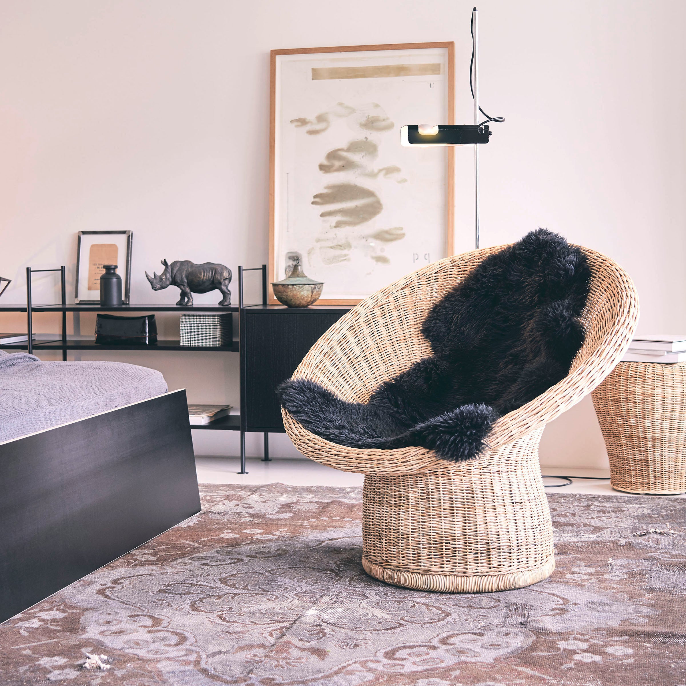 A cozy room features Richard Lamperts E10 Lounge Chair with a black fur cushion, a gray patterned rug, modern artworks, and decorative pieces. Egon Eiermanns influence shines in the minimalist design with natural and neutral tones for elegance.