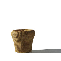 The Rattan Stool E14 by Richard Lampert, with its tall, bulbous shape, sits against a white background. The contrast of light and shadow highlights its woven texture, evoking the iconic designs of Egon Eiermann.