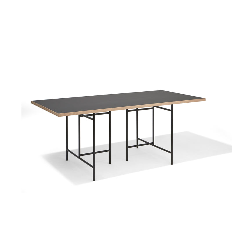 The Eiermann 3 Table by Richard Lampert features a black top with light wood edges and a thin metal frame with geometric legs. Ideal as a worktop or conference table, it stands out against a plain white background with its sleek, minimalist design.