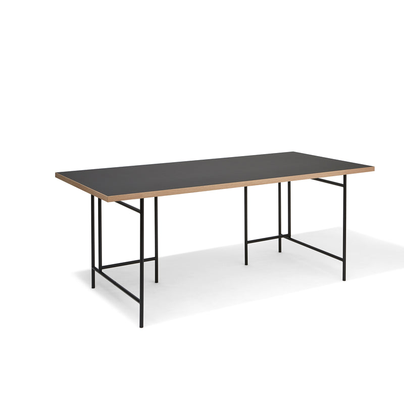The Eiermann 3 Table by Richard Lampert features a black top with thin wooden edges, evoking its classic style, and stands on minimalist black metal legs in an empty white space.