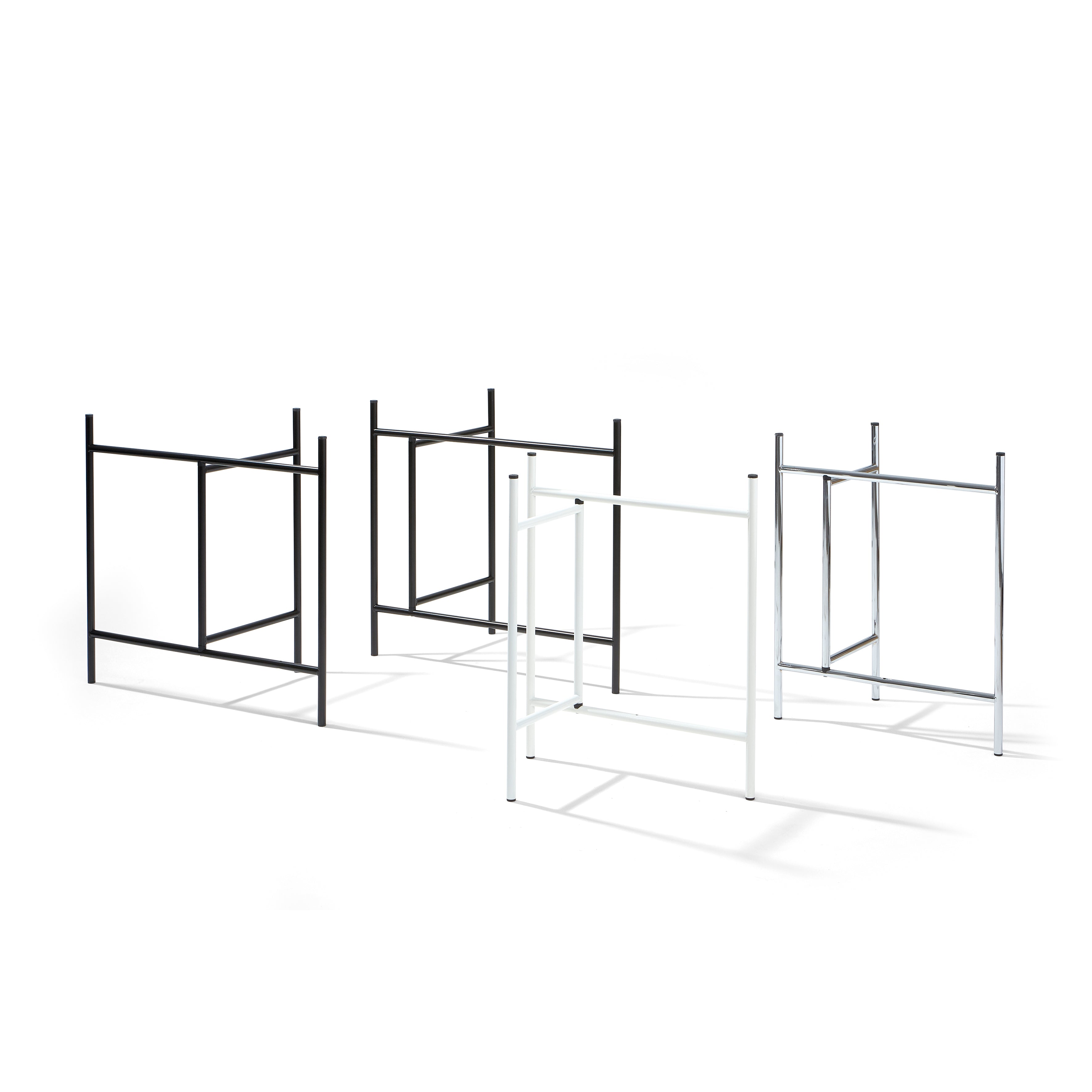 Four metal clothing racks against a white backdrop echo the sleek design of the Eiermann 3 Table by Richard Lampert. Featuring two in black and two in white, each has a rectangular frame with vertical posts and horizontal bars for stability. Shadows elegantly grace the floor beneath them.