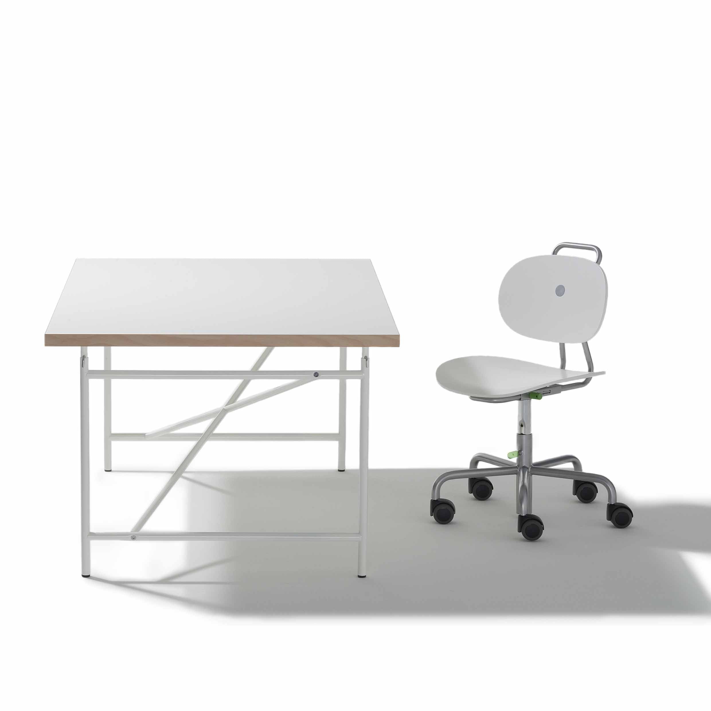 A minimalist workspace with a height-adjustable white Eiermann Kids Table by Richard Lampert, featuring a light wood edge and metal legs, paired with a white office chair on wheels that has a rounded backrest and metal frame with handle.