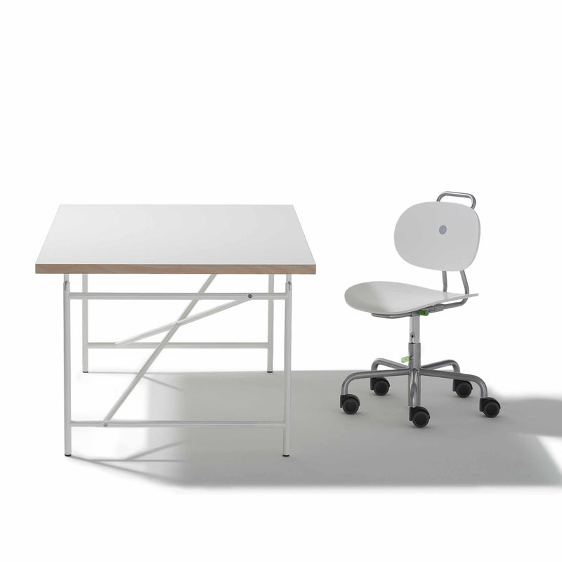 A minimalist workspace with a height-adjustable white Eiermann Kids Table by Richard Lampert, featuring a light wood edge and metal legs, paired with a white office chair on wheels that has a rounded backrest and metal frame with handle.